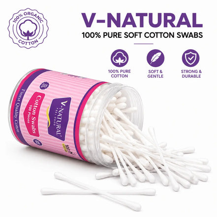 V-Natural cotton swabs in a clear plastic jar with a pink and purple label, shown tipped over with several swabs spilling out on a white background. Text and icons above read 'V-NATURAL 100% PURE SOFT COTTON SWABS' and highlight organic cotton, pure cotto